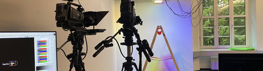 TV-Studio, zwei Kameras, farbig beleuchteter Hintergrund