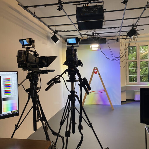 TV-Studio, zwei Kameras, farbig beleuchteter Hintergrund